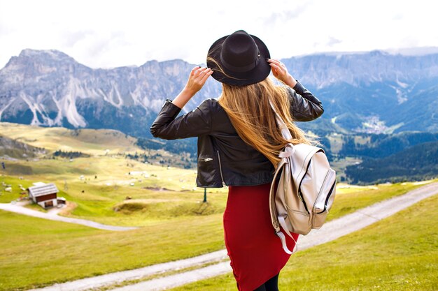 Amazing traveling experience image of beautiful stylish woman posing back and looking at breathtaking mountains view