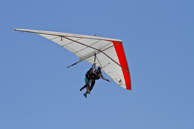 Amazing view of human flying on a hang glider isolated on a blue sky background