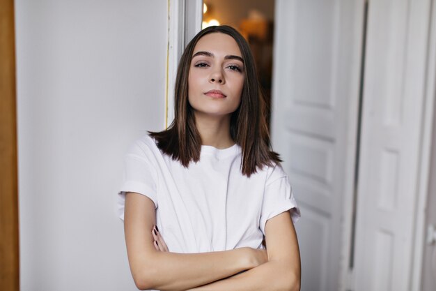 Amazing woman with nude makeup posing in her apartment. Indoor photo of caucasian charming lady standing with arms crossed.