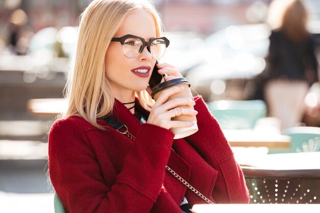 Amazing young caucasian woman talking by phone drinking coffee