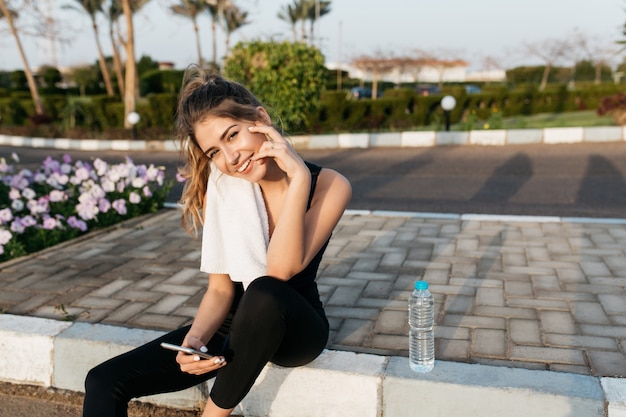 Amazing young sportswoman smiling in sunny morning on street of tropical city. Enjoying summer, expressing positivity, training, workout, motivation, cute fashionable model