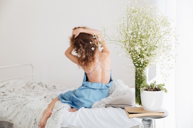 Amazing young woman sitting indoors on bed stretching