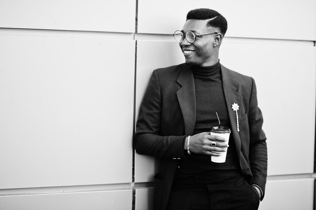 Amazingly looking african american man wear at blue blazer with brooch black turtleneck and glasses posed at street Fashionable black guy with cup of coffee