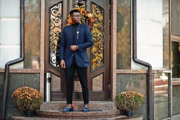 Amazingly looking african american man wear at blue blazer with brooch black turtleneck and glasses posed at street Fashionable black guy