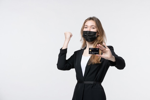 Ambitious female entrepreneur in suit wearing her medical mask and showing bank card enjoying her success on white