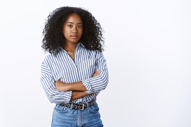 Ambitious good-looking smart creative dark-skinned girl entrepreneur determined achieve goal standing confident arms crossed looking serious self-assured camera, posing white wall