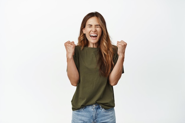 Ambitious successful woman, middle aged female winning, scream from rejoice and delight, clench fist like winner, become champion, achieve goal, celebrating victory, white background.