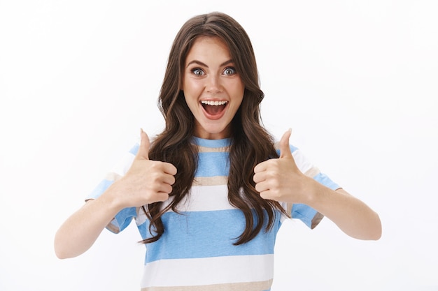 Ambitious upbeat good-looking modern woman looking satisfied, excited happily thumb-up approve awesome idea, smiling entertained and joyful, accept plan, give judgement sign, white wall