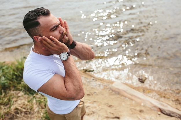 American bearded man guarda la riva del fiume con una giacca blu