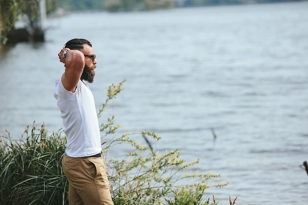 American Bearded Man은 파란색 재킷을 입고 강둑을 바라보고 있습니다.