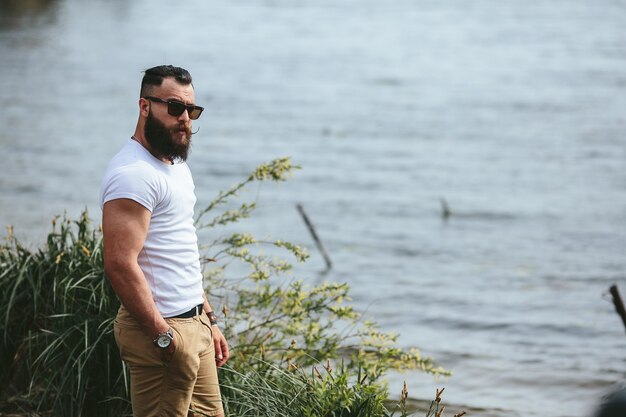 American Bearded Man looks on the river bank in a blue jacket