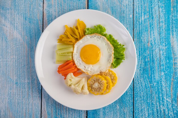 American breakfast on a blue table with fried egg, salad, pumpkin, cucumber, carrot, corn, cauliflower and tomato.