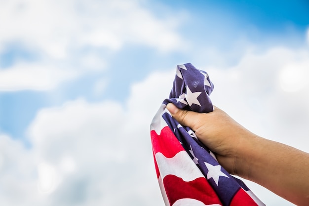 American flag held by a hand with clouds background