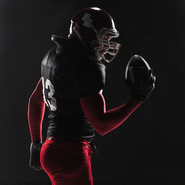 American football player posing with ball on black background