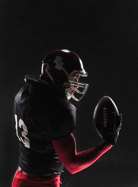 American football player posing with ball on black wall