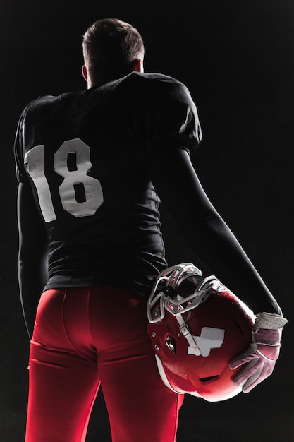Free photo american football player posing with ball on black wall