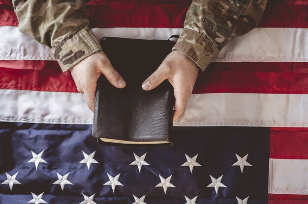 Американский солдат скорбит и молится с Библией в руках и американским флагом