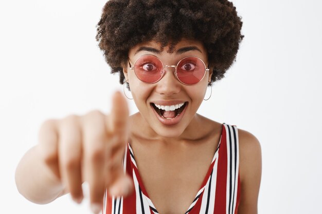 Amused attractive and stylish modern African American woman in striped blouse pulling hand towards and pointing, looking impressed and excited with awesome concept