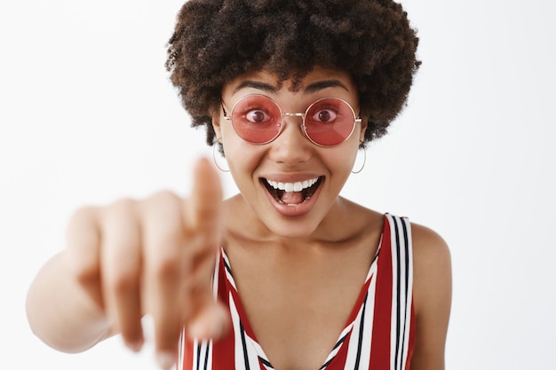 Amused attractive and stylish modern African American woman in striped blouse pulling hand towards and pointing, looking impressed and excited with awesome concept