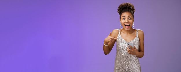 Amused charming glamour africanamerican woman in glittering silver dress astonished thrilled pointin