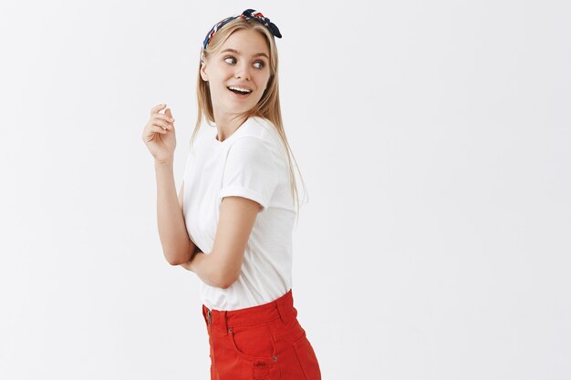 Amused and curious young blond girl posing against the white wall