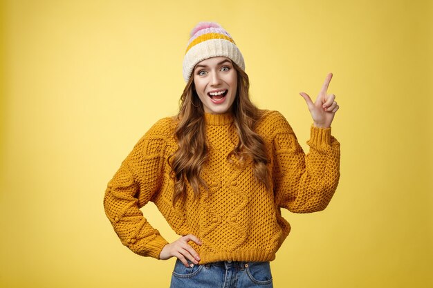 Amused friendly outgoing young girl having fun talking friends amused discussing cool promo pointing upper right corner smiling happily talking casually thrilled look camera, yellow background