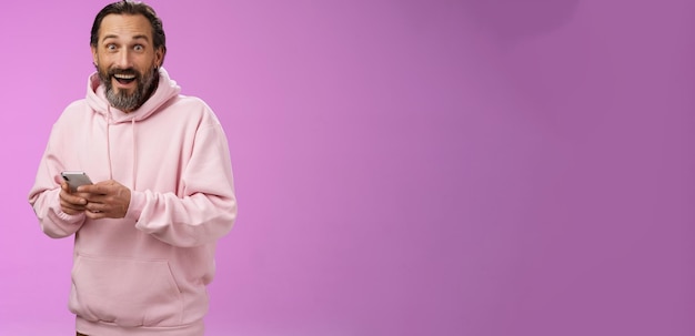 Free photo amused happy fascinated adult mature caucasian bearded man in pink hoodie gasping impressed holding