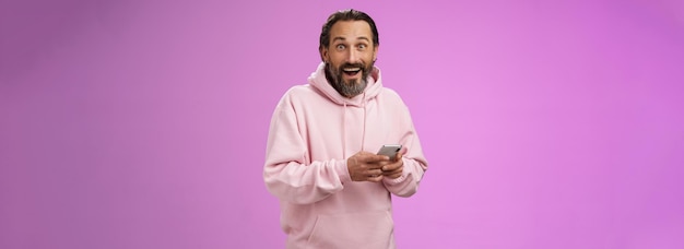 Free photo amused happy fascinated adult mature caucasian bearded man in pink hoodie gasping impressed holding