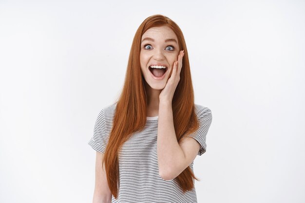 Amused happy joyful good-looking entertained redhead girl cheering touch cheek surprised widen eyes smiling amazed get good news best awesome day ever, standing white wall