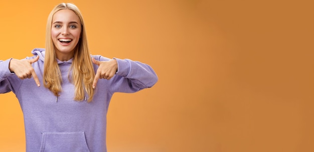 Divertimento gioioso bella ragazza bionda puntando verso il basso presente nuovo prodotto fresco sorridendo ampiamente