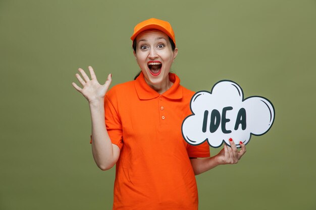 Amused middleaged delivery woman wearing uniform and cap holding idea bubble looking at camera showing empty hand isolated on olive green background