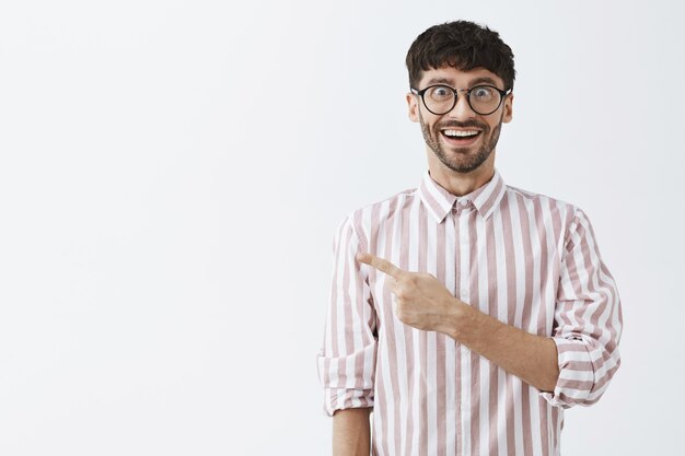 Amused stylish bearded guy posing against the white wall with glasses