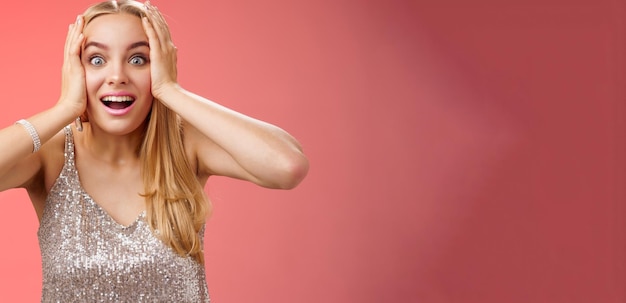 Free photo amused surprised excited young blond attractive woman in silver glittering stylish dress hold head