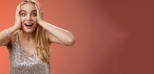 Amused surprised excited young blond attractive woman in silver glittering stylish dress hold head