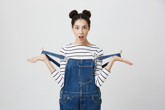 Free photo amused and surprised girl taking-off overalls straps and look amazed