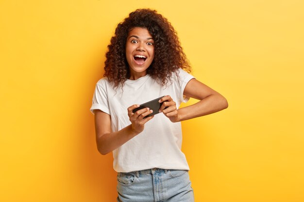 Amused young woman with curly hair posing with her phone