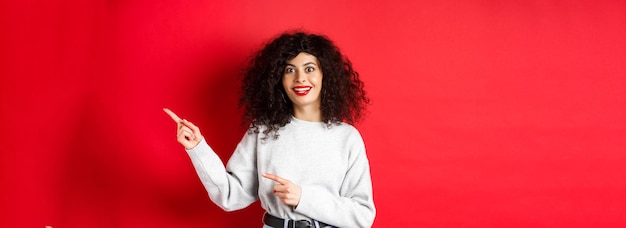 Free photo amused young woman with curly hairstyle pointing fingers right at logo looking impressed and excited