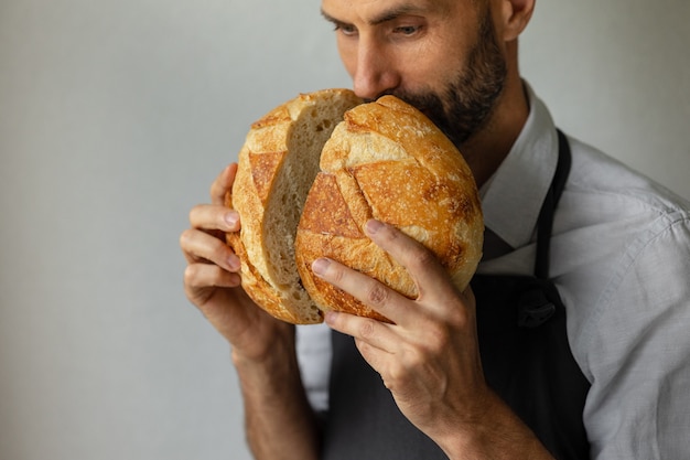 大人​の​ヨーロッパ​の​男性​の​パン屋​は​彼​の​手​で​丸い​焼きたて​の​パン​を​持っています​パン屋​の​男性​は