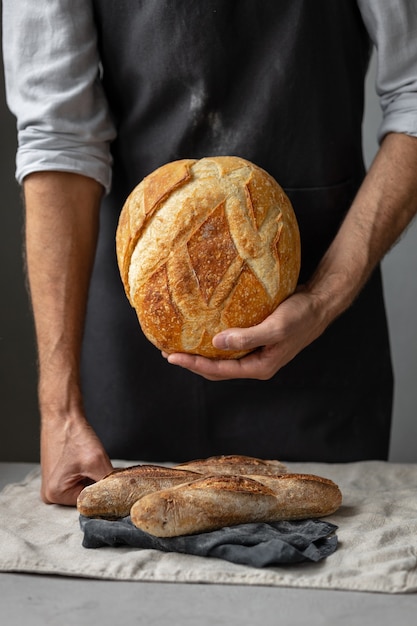 大人のヨーロッパの男性のパン屋は彼の手で丸い焼きたてのパンを持っていますパン屋の男性は Premium写真