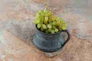 Бесплатное фото Древняя чашка, полная сладкого винограда на мраморном столе.