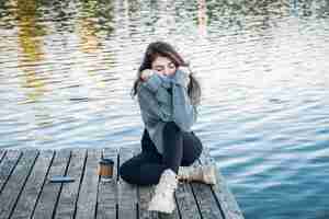 無料写真 セーターを着た魅力的な若い女性が川のそばに座っている