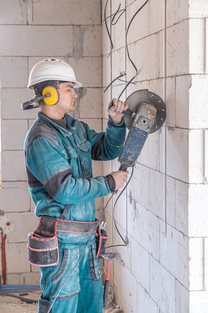 Бесплатное фото Электрик-строитель в защитном шлеме на рабочем месте работает с болгаркой.