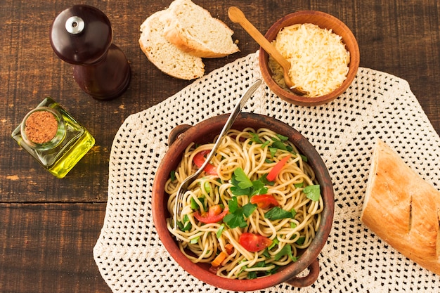 Бесплатное фото Верхний вид спагетти-пасты на глиняной посуде с сыром и хлебом на деревянном столе