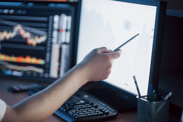 Analyzing data. Close-up of young businessman pointing on the data presented in the chart with pen while working in creative office