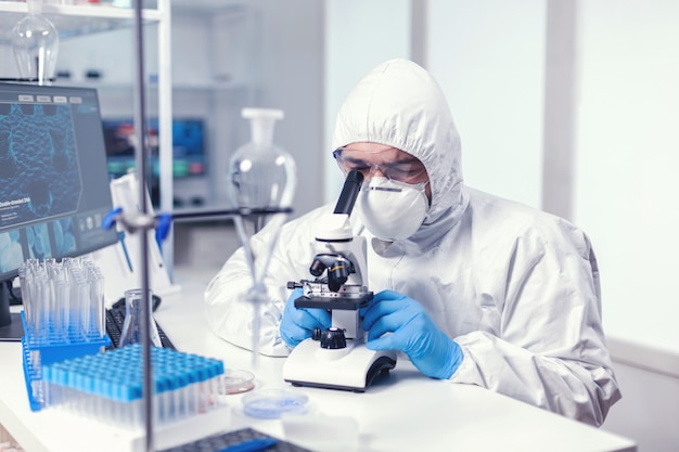 Analyzing virus in microbiology lab using microscope wearing ppe suit and glasses