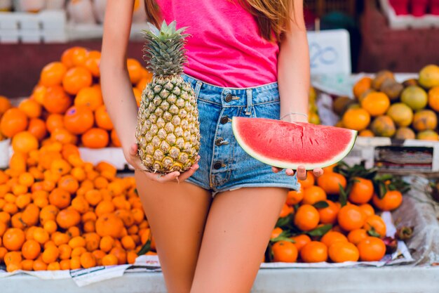 Ananas and slice of watermelon in hands of girl on tropical fruits market