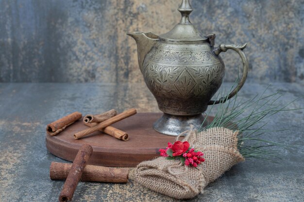 Ancient kettle with cinnamon sticks on wooden plate.