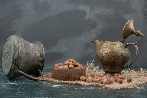 Древний чайник с деревянной тарелкой орехов на мраморном фоне