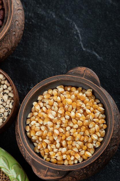 An ancient pot with uncooked popcorn on a dark