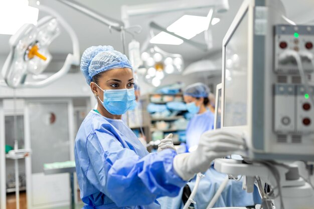 Anesthetist Working In Operating Theatre Wearing Protecive Gear checking monitors while sedating patient before surgical procedure in hospital